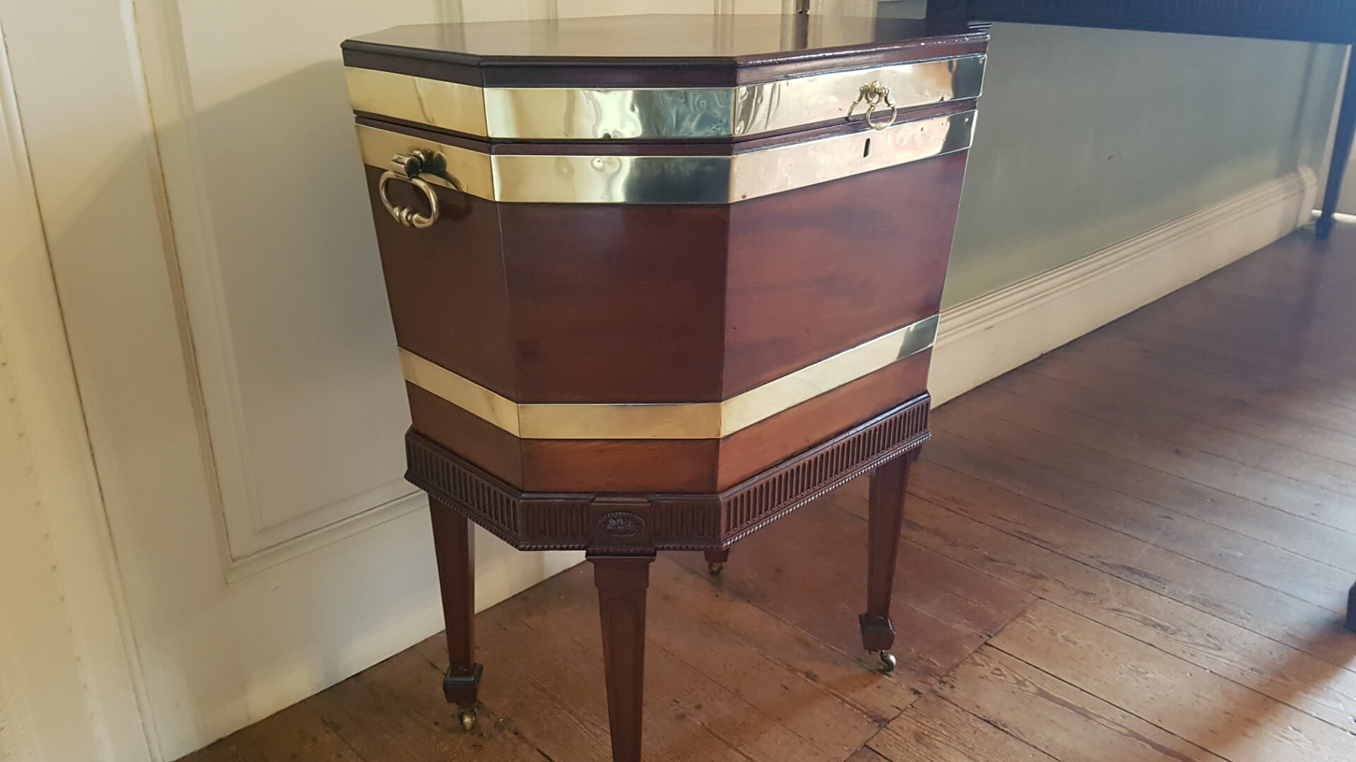 A Georgian cellarette - an octagonal mahogany box on legs banded in brass with ring handles at the end.