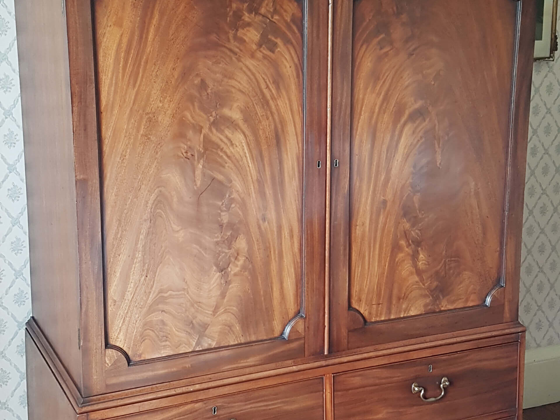 A Gelrogain clothes press by Thomas Chippendale. the upper double doored cupboard has panels of finest flame mahogany set above drawers with brass handles