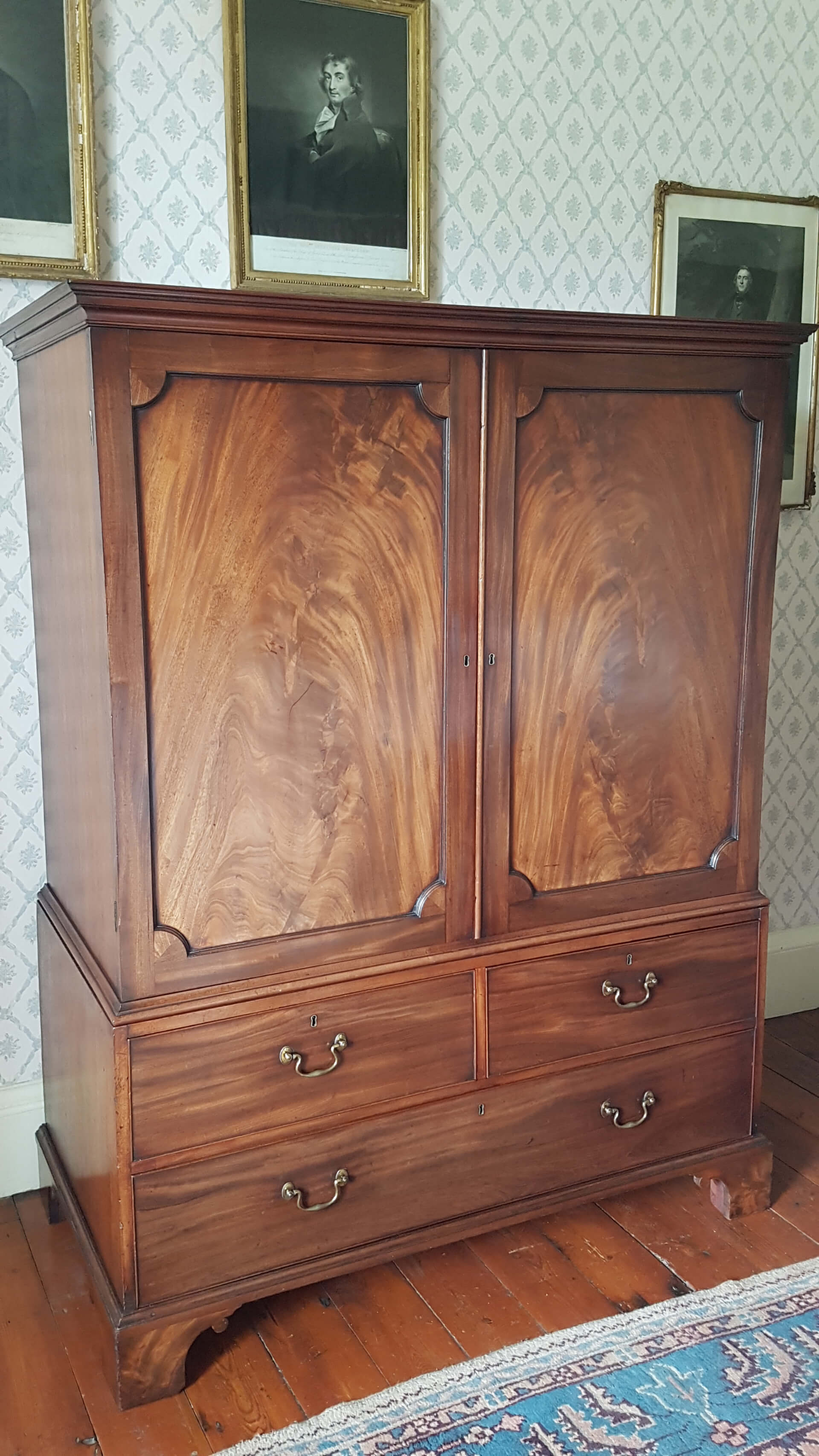 A Gelrogain clothes press by Thomas Chippendale. the upper double doored cupboard has panels of finest flame mahogany set above drawers with brass handles