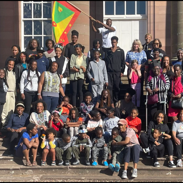 Image of a group of adults and children on the steps of Paxton House waving the Grenadian flag
