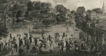 A black and white engraving shows a busy market place in st Georges, Grenada about 1790. In the left centre, a group of British soldier stand to attention in a square. In the foreground a group of civilians of all sexes and races mingle. The men wear frock coats and the women wear caps and muslin dresses. Market traders sit on the ground to display their goods or carry them on their heads. In the background, simple two storey houses climb up the hills until it gives way to forest