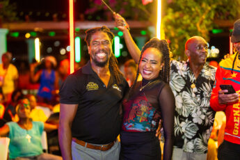 A couple celebrate independence at a party on Grenada. They are gunning broadly and waving a flag.