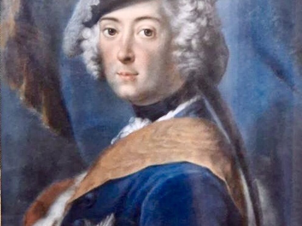 A portrait of an eighteenth century gentleman in a powdered wig under a tricorn hat with a giant white feather. He wars a blue uniform iwht a red silk sash and a large jewelled star on his breast. the background is of swirling drapery in blue. This is Frederick the Great of Prussia by the Italian pastellist Rosalba Carriere.