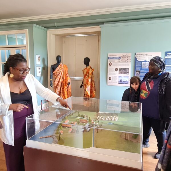 A group of people looking at a 3d model of the estates in Grenada. In the background you can see two models and information panels on the walls. This is in the dedicated exhibition space in Paxton House.