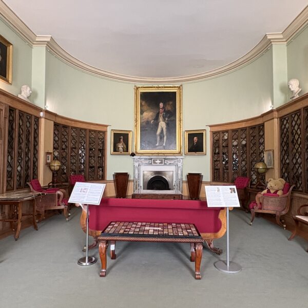 Image of the library showing cases of books and furniture by William Trotter. The upholstered furniture in this room is dark red.