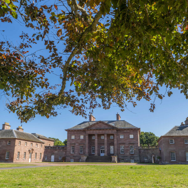 Paxton House on a summers day. Blue skies and leaves from a tree are in the frame
